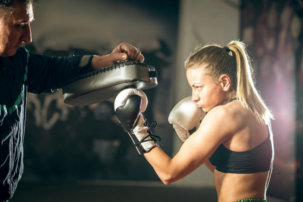 Girl practicing boxing at the gym with the help of his coach