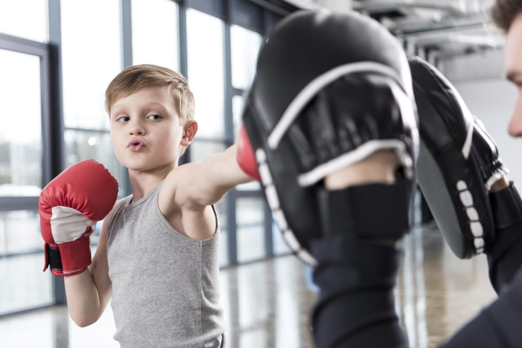 Little child practicing boxing at the gym with the help of his coach